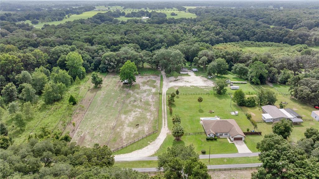 An aerial view shows a house with a pool, a dirt driveway, and fenced pastures — 13783 SE 8TH COURT, OCALA, FL