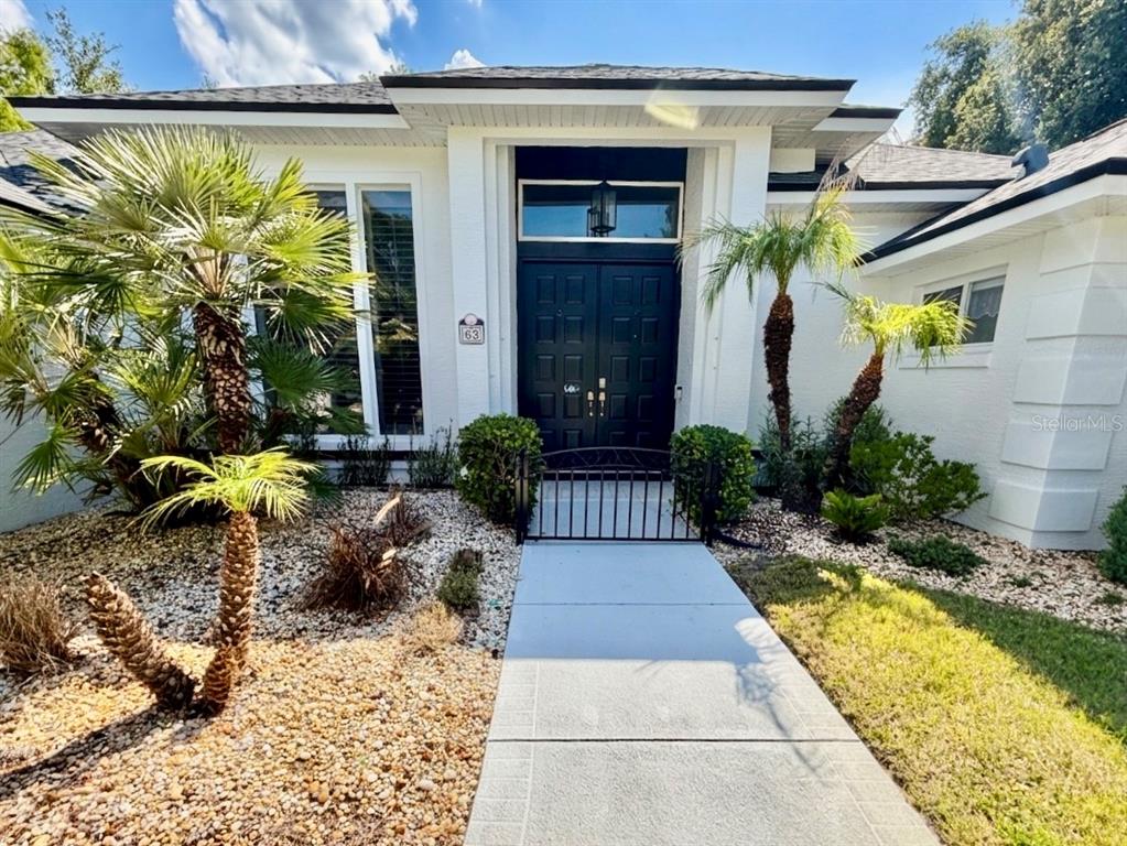 A white house exterior features a black double door entrance with a small metal gate — 63 BAY LAKE DRIVE, ORMOND BEACH, FL