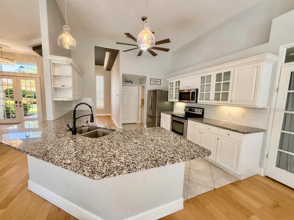 A kitchen features white cabinetry, granite countertops, a central island, and light wood flooring — 63 BAY LAKE DRIVE, ORMOND BEACH, FL