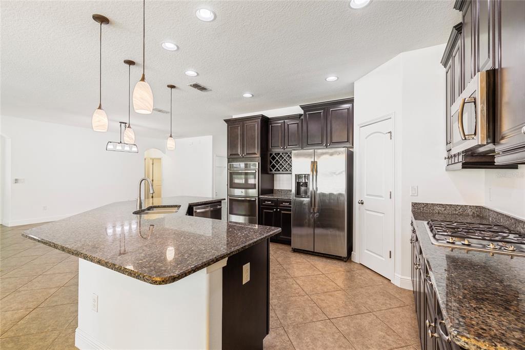 A kitchen features dark wood cabinets, granite countertops, stainless steel appliances, and a central island — 6706 RIVERSIDE BLUFFS DRIVE, RIVERVIEW, FL