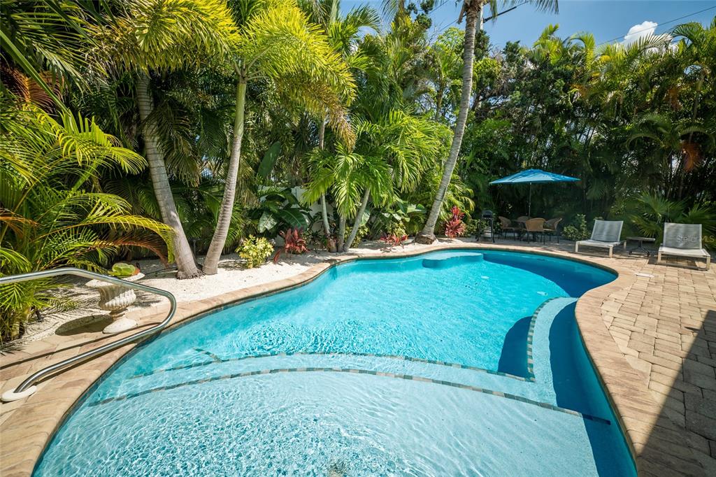A backyard swimming pool with a sun shelf, stone pavers, and lush tropical landscaping — 324 64TH STREET, HOLMES BEACH, FL