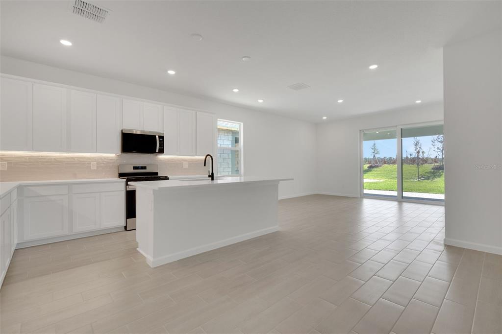 A modern kitchen with white cabinets, a central island, and tile flooring opens to a patio — 5412 NW CAMBERLY COURT, PORT ST LUCIE, FL
