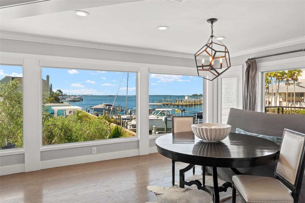 A dining area features a round table, upholstered seating, and large windows overlooking a marina — 439 CAUSEWAY BOULEVARD, DUNEDIN, FL
