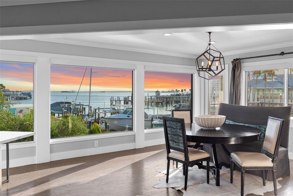 A dining area with a round table and chairs overlooks a marina at sunset — 439 CAUSEWAY BOULEVARD, DUNEDIN, FL