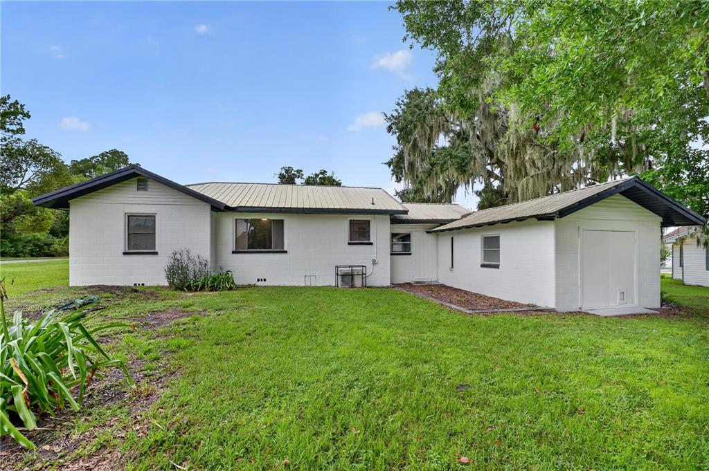 The exterior of a white concrete block house with a metal roof and green lawn — 5514 SE HAMES ROAD, BELLEVIEW, FL
