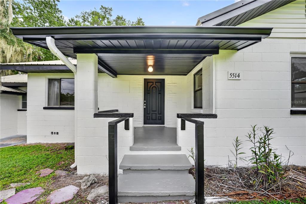 The exterior of a white concrete block house features a covered porch and black door — 5514 SE HAMES ROAD, BELLEVIEW, FL