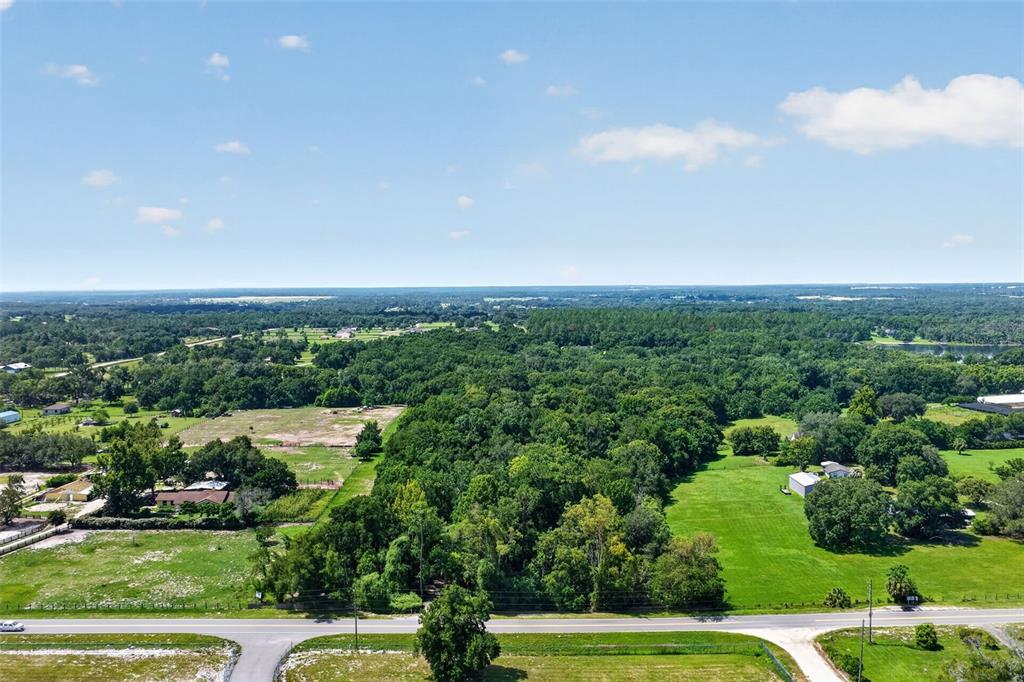 An aerial view shows a large, wooded lot bordered by a road and open fields — 22740 COUNTY ROAD 44A, EUSTIS, FL