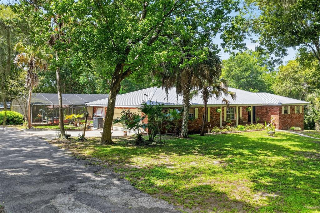 A single-story brick house with a metal roof and an attached screened-in patio area — 22740 COUNTY ROAD 44A, EUSTIS, FL