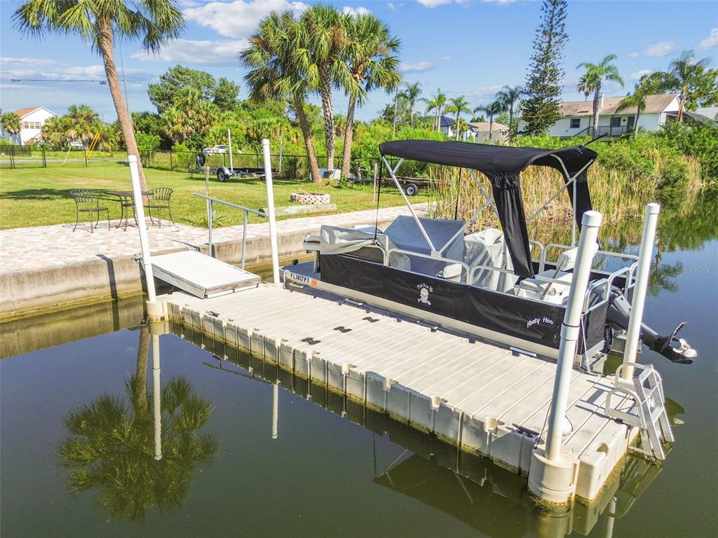 A pontoon boat is docked at a floating pier next to a grassy backyard — 3314 FERNLEAF DRIVE, HERNANDO BEACH, FL