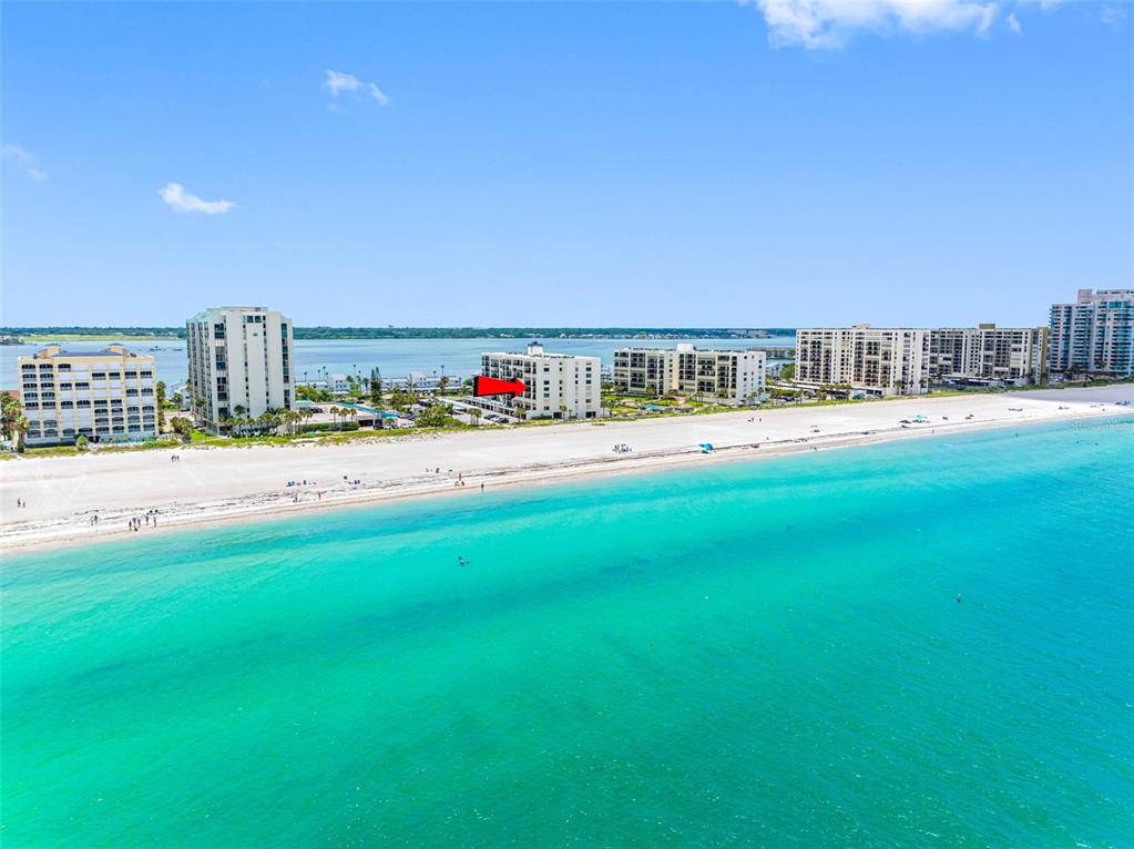 An aerial view shows a white beachfront condominium building marked with a red arrow — 1400 GULF BOULEVARD UNIT 409, CLEARWATER BEACH, FL