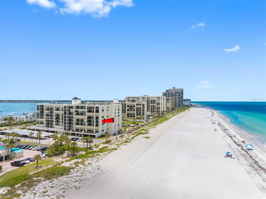 An aerial view shows a multi-story beachfront condominium building with a red arrow pointing toward it — 1400 GULF BOULEVARD UNIT 409, CLEARWATER BEACH, FL