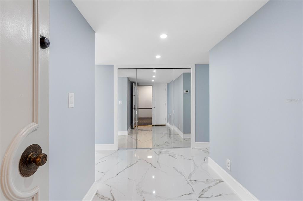 A hallway features light blue walls, white marble-patterned tile flooring, and mirrored closet doors — 1400 GULF BOULEVARD UNIT 409, CLEARWATER BEACH, FL