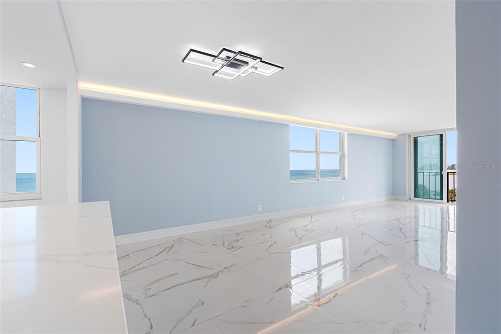 A bright, open-plan living area features light blue walls, marble-patterned tile floors, and ocean views — 1400 GULF BOULEVARD UNIT 409, CLEARWATER BEACH, FL
