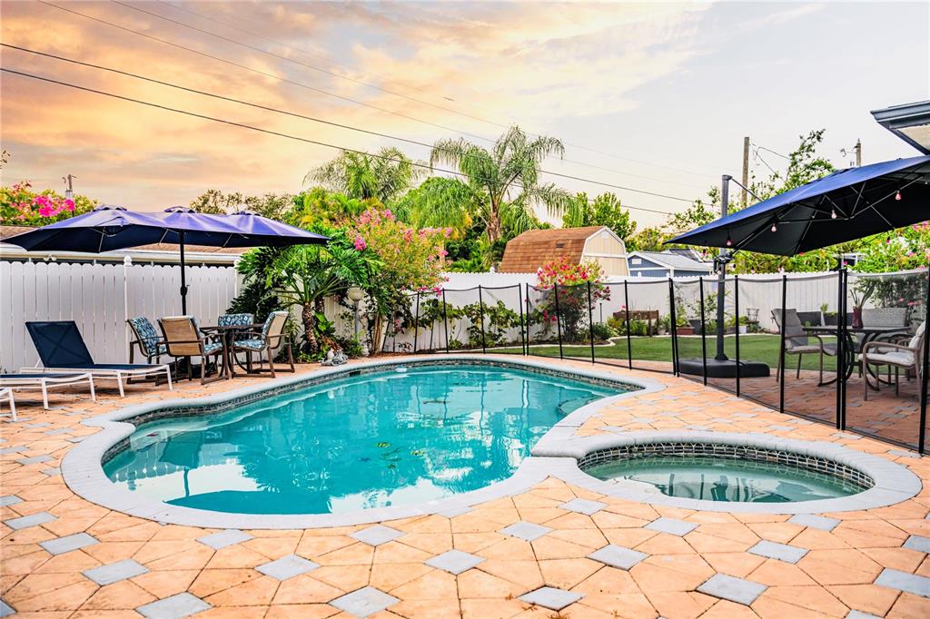A backyard swimming pool and attached spa are surrounded by a paved patio and umbrellas — 898 CORVETTE DRIVE, LARGO, FL