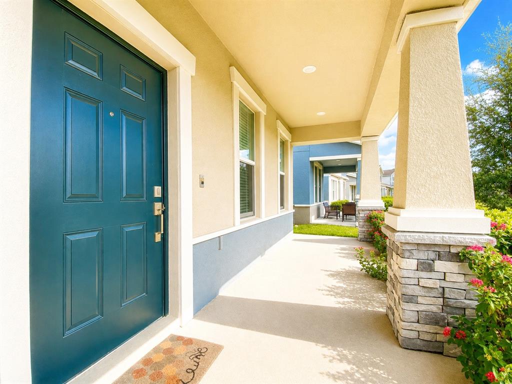 A teal front door opens onto a covered porch with stone-based columns and a welcome mat — 11018 SILVER SURFER ALLEY, WINTER GARDEN, FL