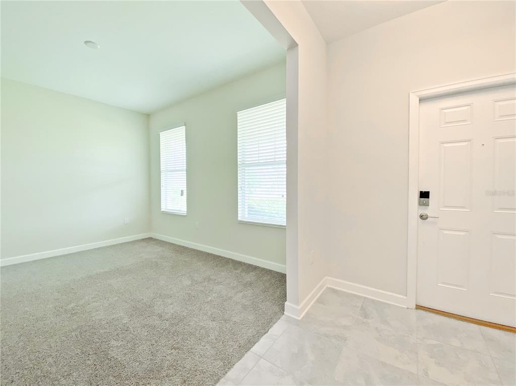 A room with gray carpet and two windows next to a tiled entryway with a door — 11018 SILVER SURFER ALLEY, WINTER GARDEN, FL