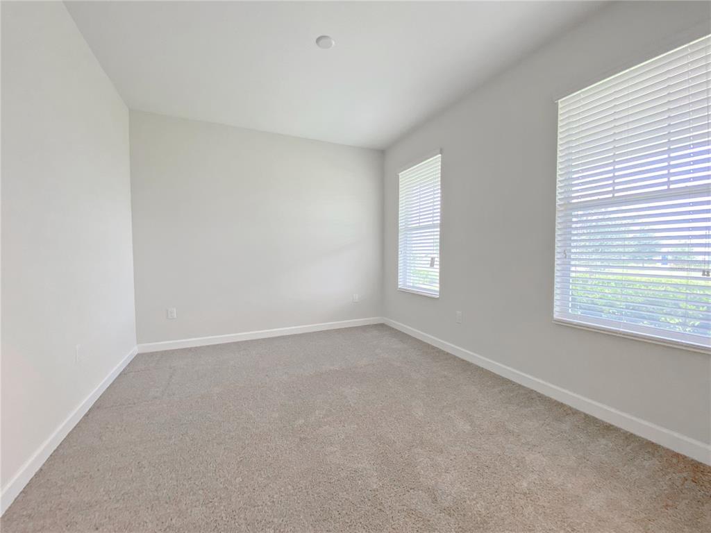 An empty bedroom features light gray walls, beige carpeting, and two windows with white blinds — 11018 SILVER SURFER ALLEY, WINTER GARDEN, FL