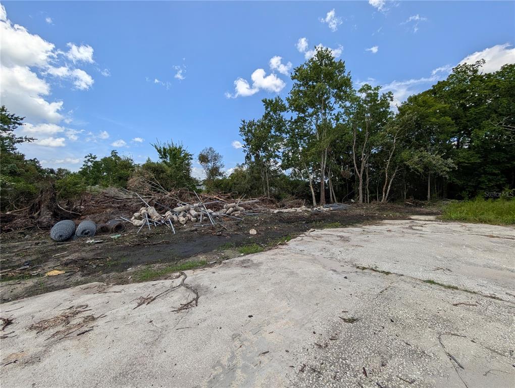 A concrete slab sits next to a pile of debris and trees under a blue sky — 18847 JEFFERSON AVENUE, ORLANDO, FL