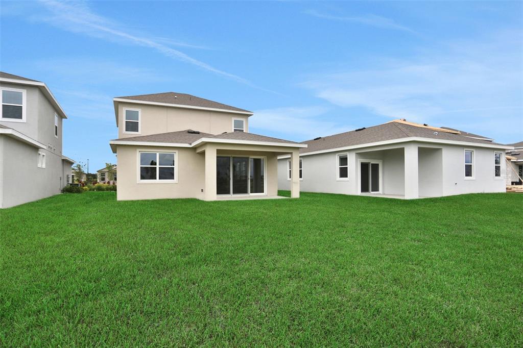 The rear exterior of two suburban houses features beige stucco siding, covered patios, and lawns — 8112 SUNNY POINT TRAIL, PARRISH, FL