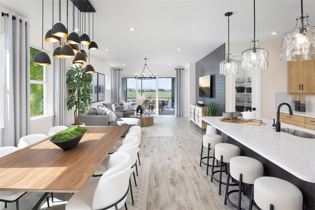 An open-concept living, dining, and kitchen area with wood-look tile floors and modern light fixtures — 11423 BOUNDLESS TERRACE, VENICE, FL