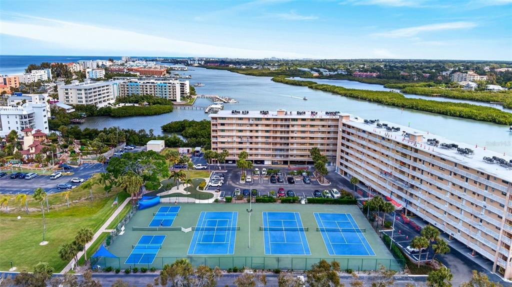 A balcony with blue chairs overlooks a grassy lawn, dense trees, and distant apartment buildings — 19451 GULF BOULEVARD UNIT 204, INDIAN SHORES, FL