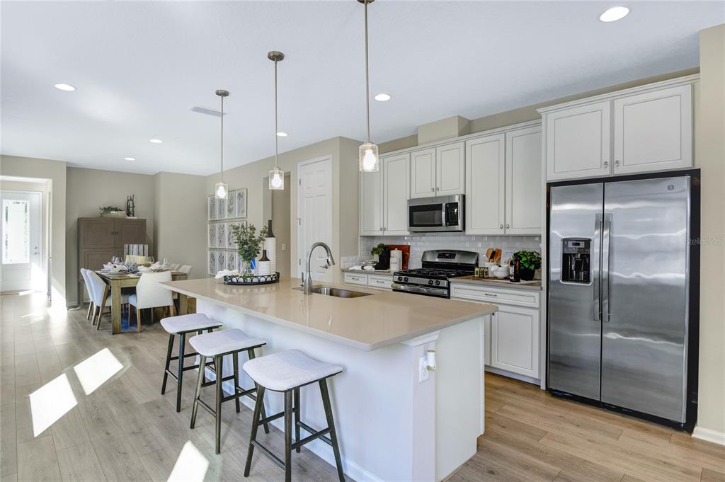 A modern kitchen features white cabinets, stainless steel appliances, a quartz island, and bar seating — 5316 SPRING MAIDEN CIRCLE, APOLLO BEACH, FL