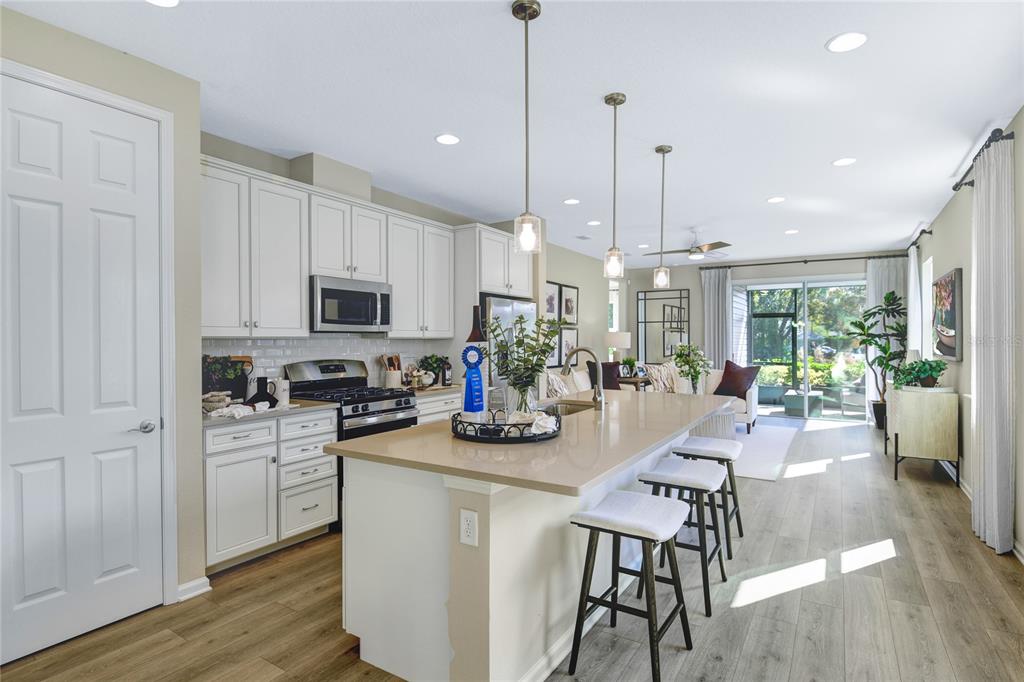 A modern kitchen features white cabinets, a large quartz island with bar seating, and wood-look flooring — 5316 SPRING MAIDEN CIRCLE, APOLLO BEACH, FL