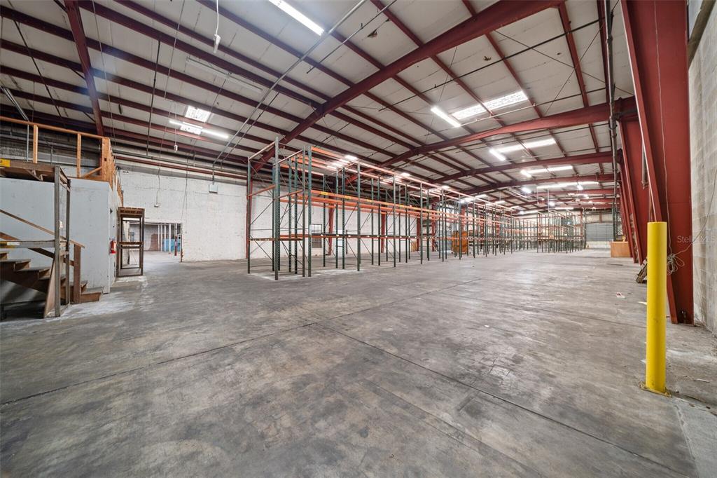 A large warehouse interior features high ceilings, exposed red steel beams, and metal storage racks — 506 SE 3RD AVENUE, OCALA, FL