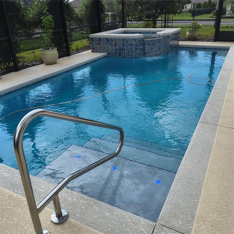 A rectangular swimming pool with an attached tiled spa and a metal handrail — 9508 SW 66TH LOOP, OCALA, FL