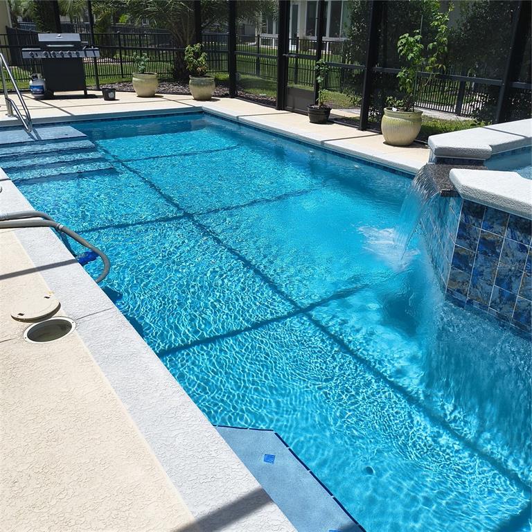A rectangular swimming pool with a waterfall feature sits inside a screened-in patio enclosure — 9508 SW 66TH LOOP, OCALA, FL