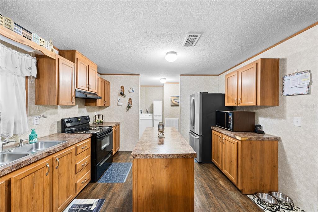 A kitchen with wood cabinets, a central island, and black appliances on wood-look flooring — 21 NE 69TH COURT, OCALA, FL