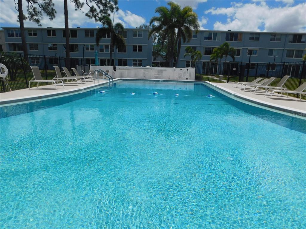 A rectangular swimming pool with lounge chairs on the deck and apartment buildings in the background — 4715 BAY STREET NE UNIT 119, ST PETERSBURG, FL