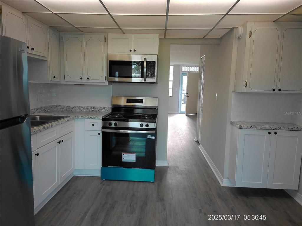 A kitchen features white cabinets, stainless steel appliances, granite countertops, and light wood-look flooring — 4715 BAY STREET NE UNIT 119, ST PETERSBURG, FL