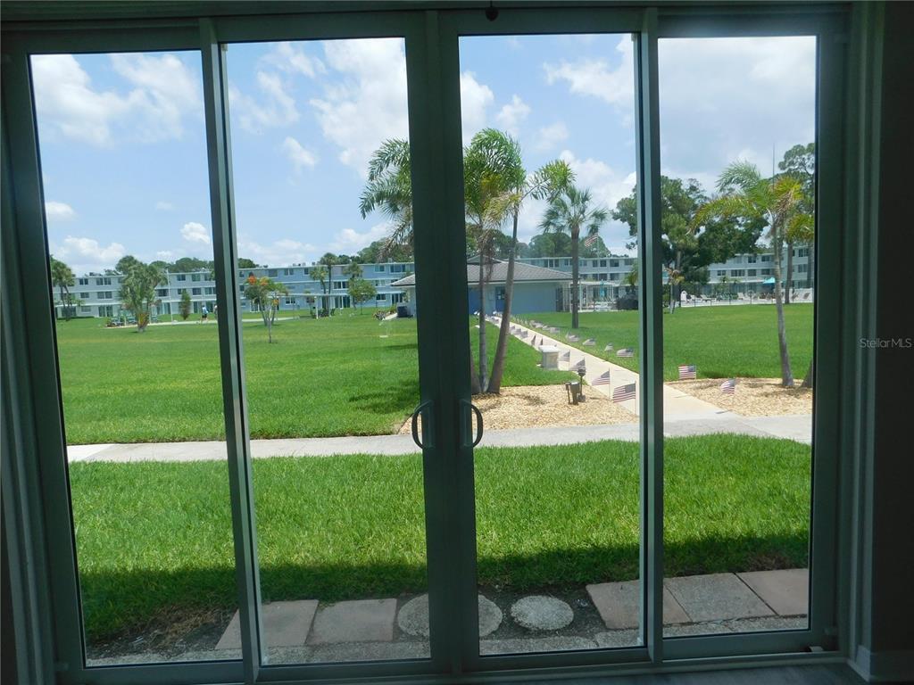 A view of a grassy courtyard and apartment buildings through large sliding glass doors — 4715 BAY STREET NE UNIT 119, ST PETERSBURG, FL