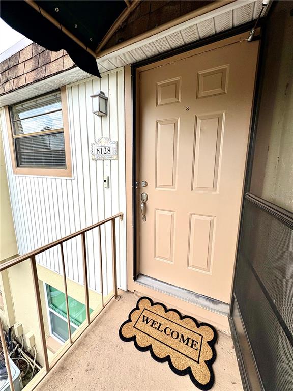 An exterior view of a tan front door with a welcome mat on a balcony — 6128 TOPHER TRAIL UNIT 6128, MULBERRY, FL