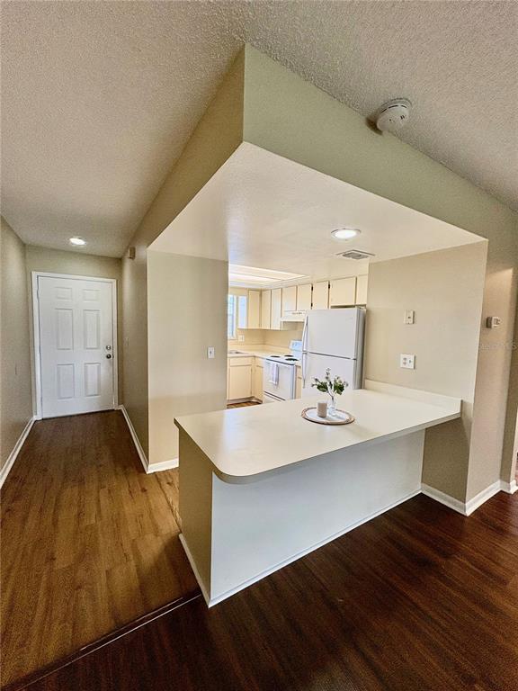 A kitchen with white appliances and a breakfast bar overlooks a hallway with wood flooring — 6128 TOPHER TRAIL UNIT 6128, MULBERRY, FL