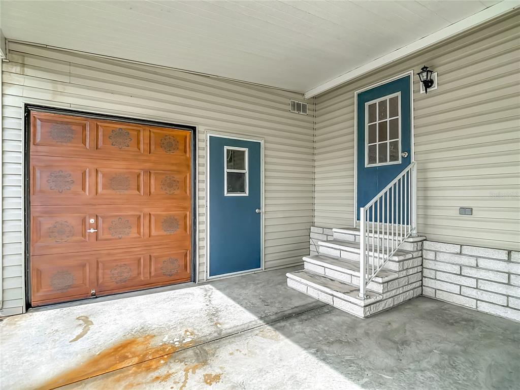 A covered concrete carport leads to a house entrance with white brick steps and siding — 5745 PAWNEE STREET, ZEPHYRHILLS, FL