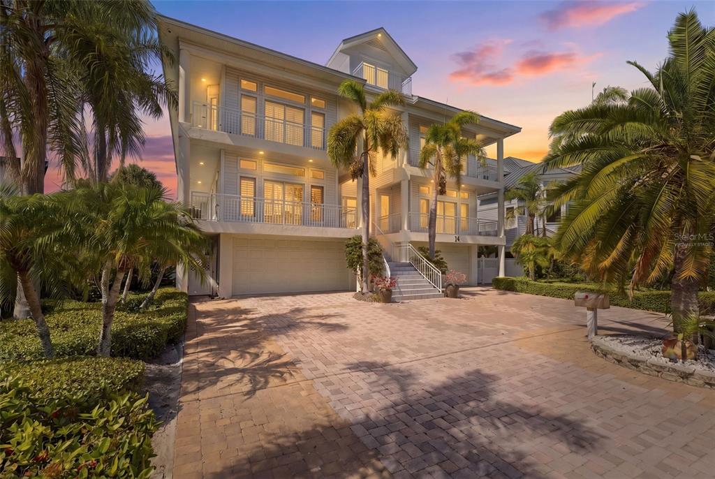 A three-story coastal home with a paved driveway, palm trees, and a front staircase — 24 N PINE CIRCLE, BELLEAIR, FL