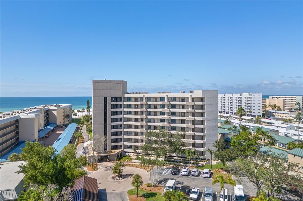 An aerial view shows a multi-story apartment building near the beach with a parking lot — 5880 MIDNIGHT PASS ROAD UNIT 704, SARASOTA, FL
