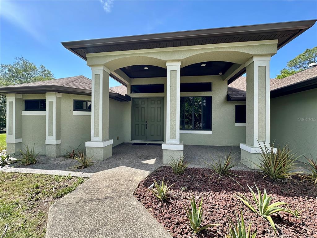 The exterior of a light green house features a covered entryway with white support columns — 7759 ESTATES DRIVE, NORTH PORT, FL