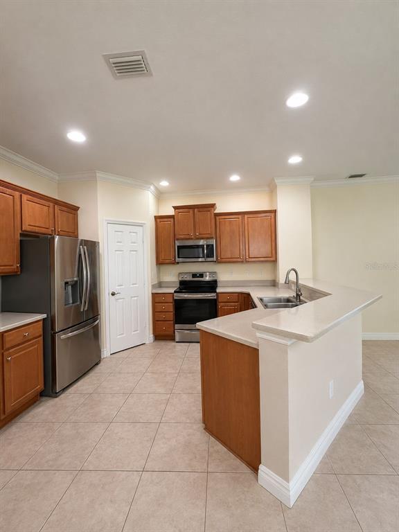 A kitchen with wood cabinets, stainless steel appliances, and a peninsula counter on tile flooring — 11505 52ND COURT E, PARRISH, FL