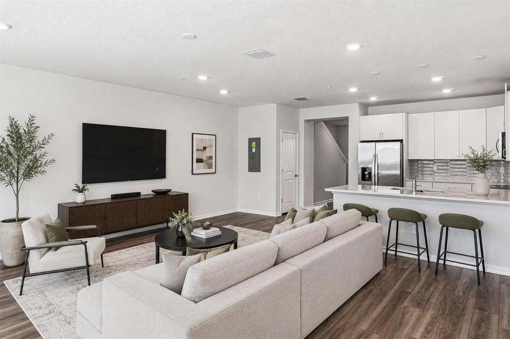 An open-concept living room and kitchen featuring a large sofa, television, and breakfast bar seating — 14375 SAPELO BEACH DRIVE, ORLANDO, FL