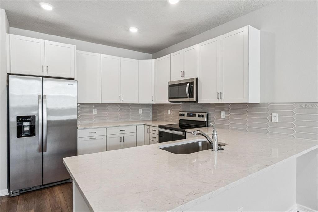 A modern kitchen features white cabinets, stainless steel appliances, and a light-colored quartz countertop — 14375 SAPELO BEACH DRIVE, ORLANDO, FL
