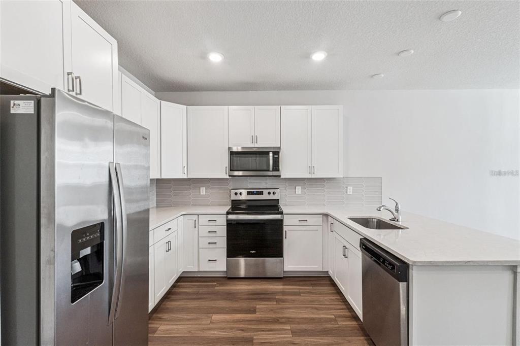 A modern kitchen features white cabinets, stainless steel appliances, quartz countertops, and wood-look flooring — 14375 SAPELO BEACH DRIVE, ORLANDO, FL
