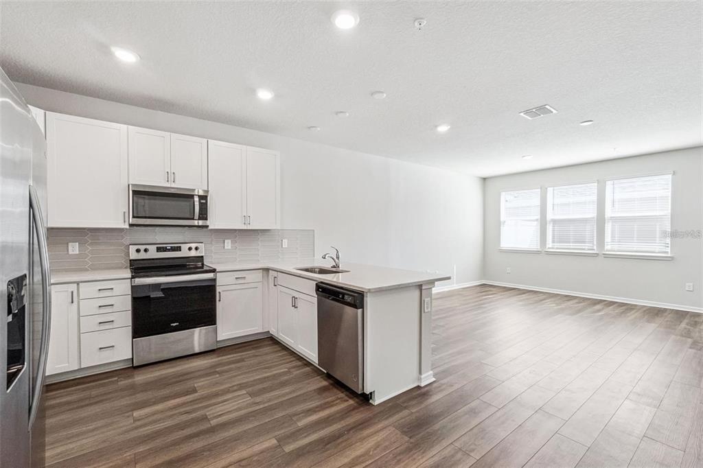 A modern kitchen with white cabinets, stainless steel appliances, and wood-look flooring — 14375 SAPELO BEACH DRIVE, ORLANDO, FL