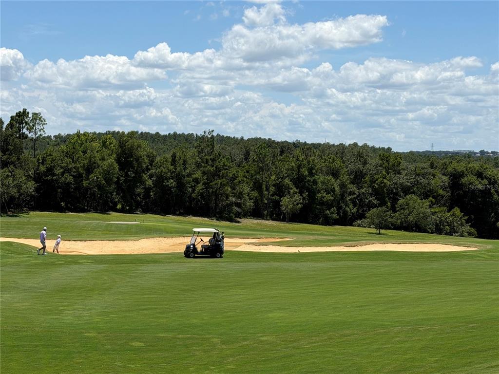 A golf course features a sand bunker, a golf cart, and two people walking nearby — 16038 VETTA DRIVE, MONTVERDE, FL