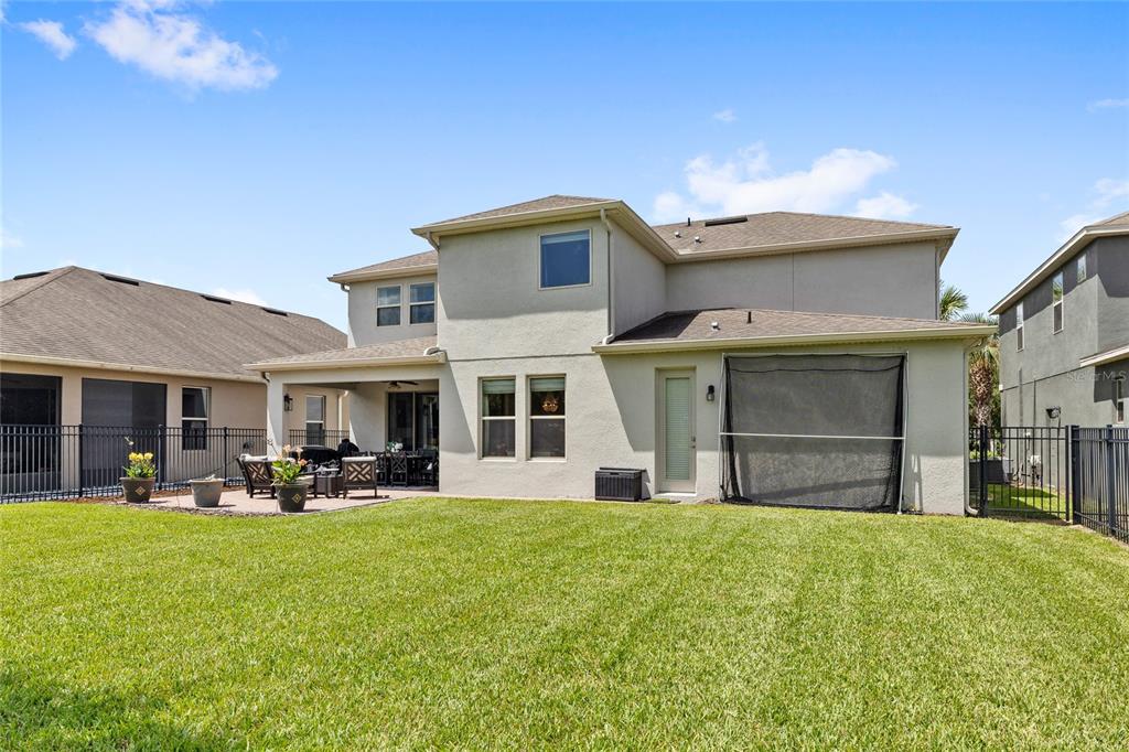 A grassy backyard features a black metal fence, mature trees, and manicured shrubs — 15671 MARINA BAY DRIVE, WINTER GARDEN, FL