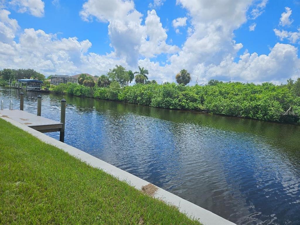 A grassy lawn borders a canal with a wooden dock and dense vegetation across the water — 3604 COMO STREET, PORT CHARLOTTE, FL