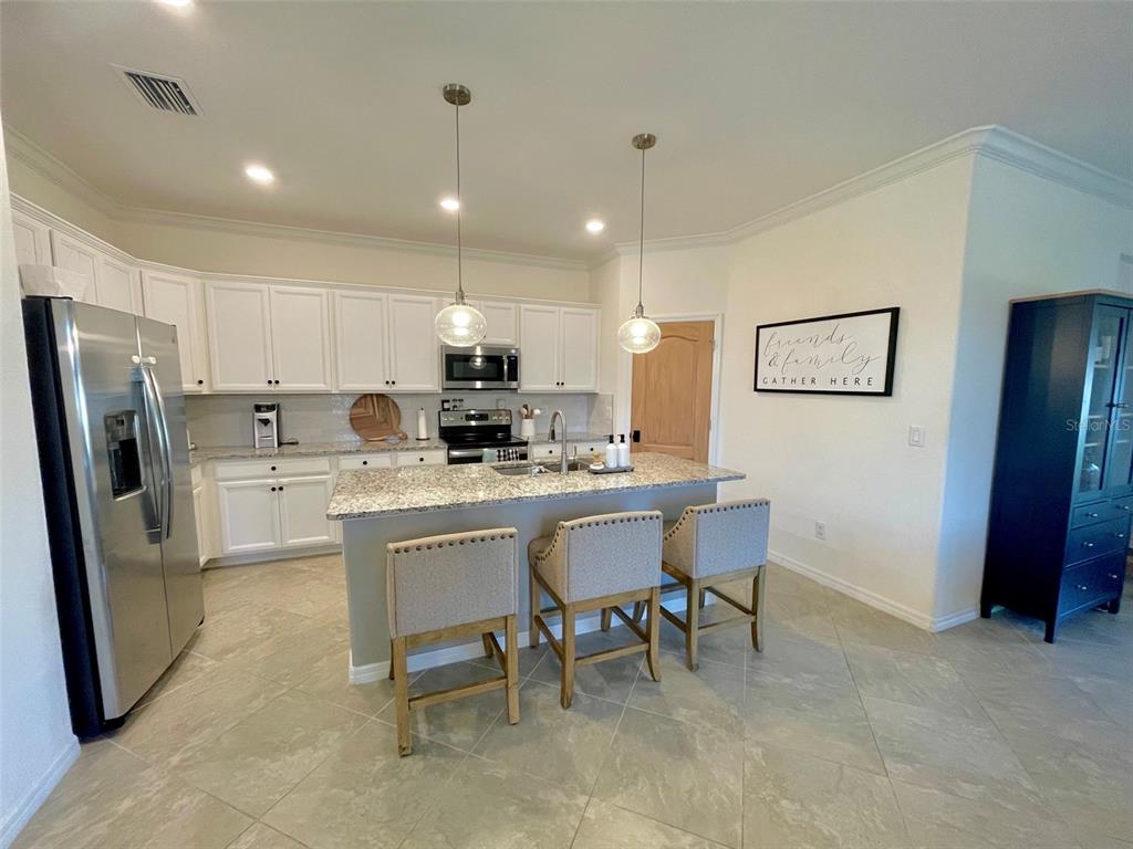A kitchen features white cabinets, granite countertops, a central island with three stools, and stainless appliances — 531 FIRE BUSH COURT, BRADENTON, FL