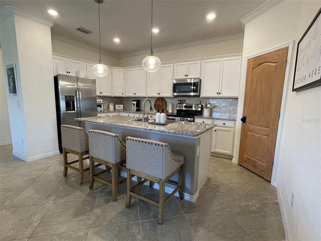 A kitchen features white cabinets, granite countertops, a central island with three chairs, and tile flooring — 531 FIRE BUSH COURT, BRADENTON, FL